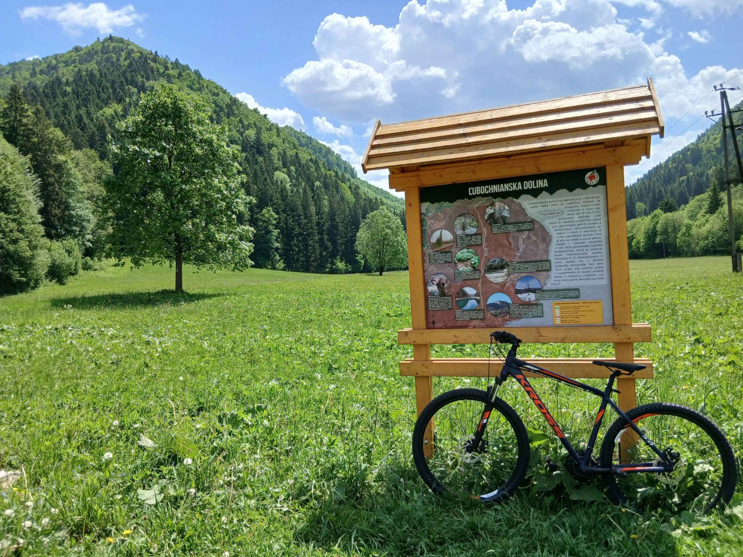 Lúka s informačnou tabuľou Ľubochnianska dolina a bicyklom v popredí